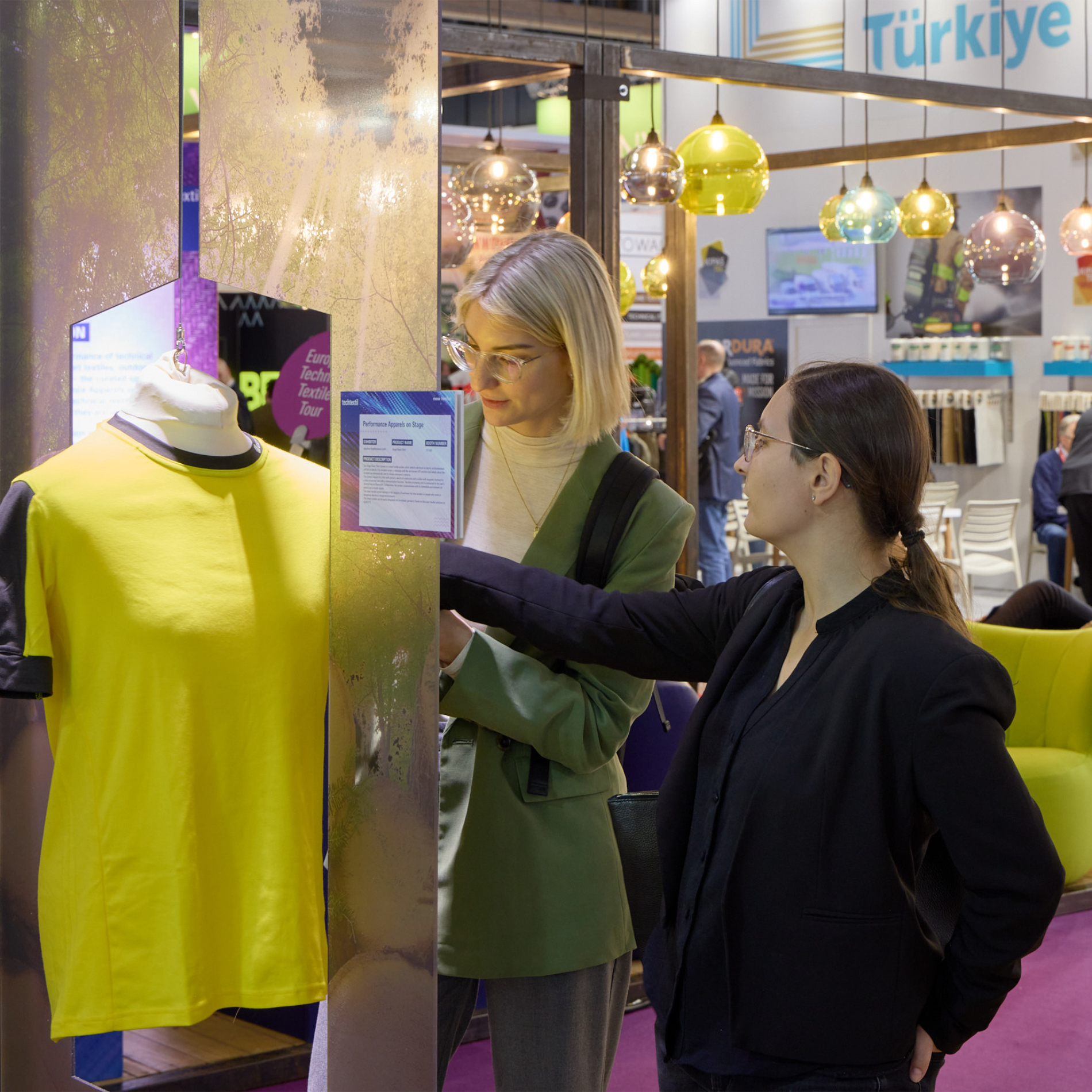 Besucherinnen auf der Messe schauen sich ein T-Shirt an